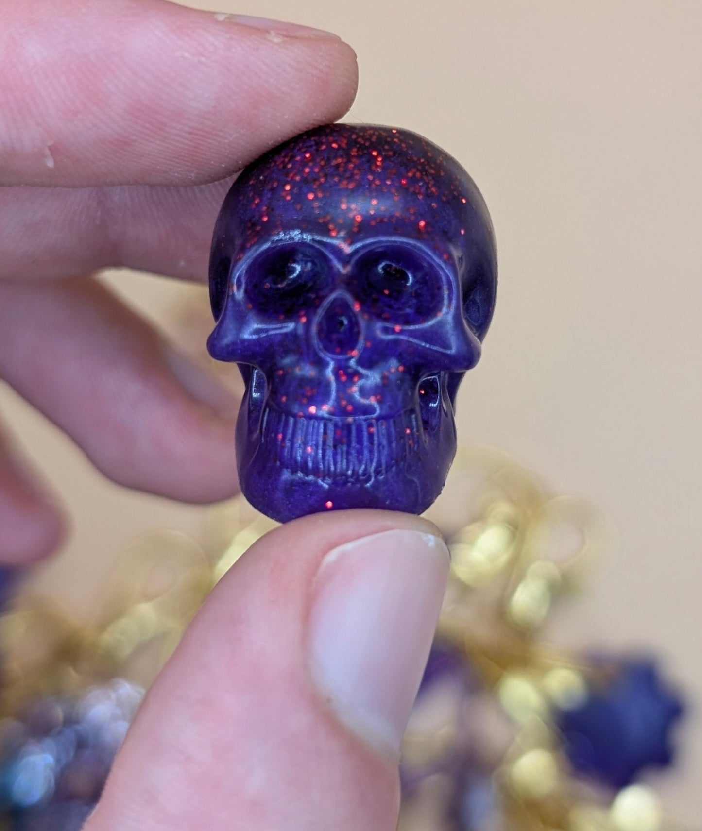 Purple glittery skull-shaped object held between fingers with a blurred background